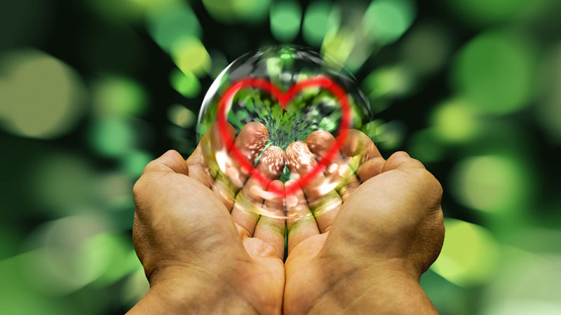 Cupped hands holding a bubble with a red heart inside of it.